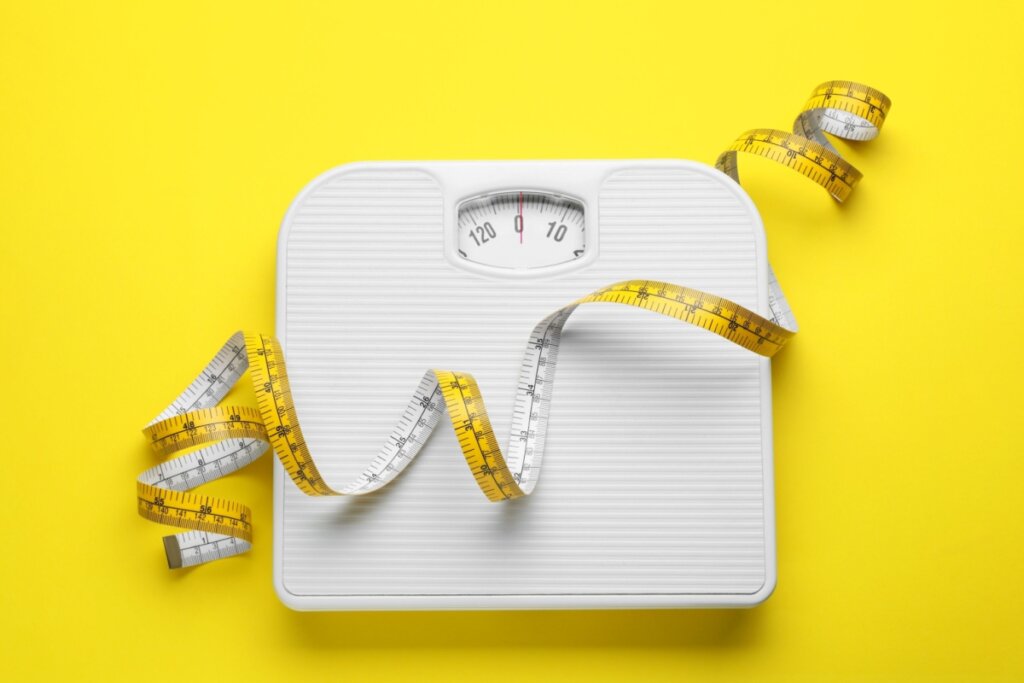 balança branca com fita métrica amarela em cima sobre fundo amarelo