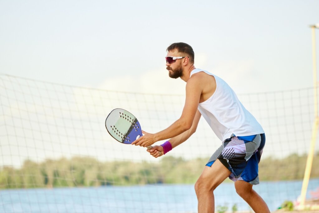 Homem jogando beach tennis na areia em posição de preparo com a raquete em mãos