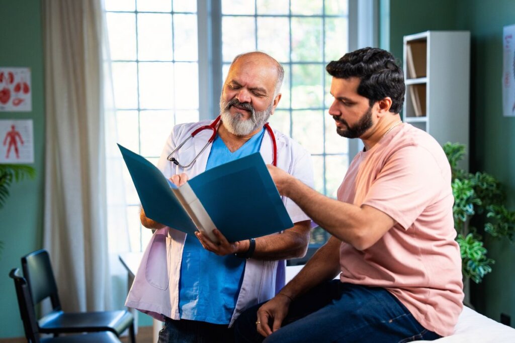 Homem sentado e um médico em pé ao lado mostrando exame para ele
