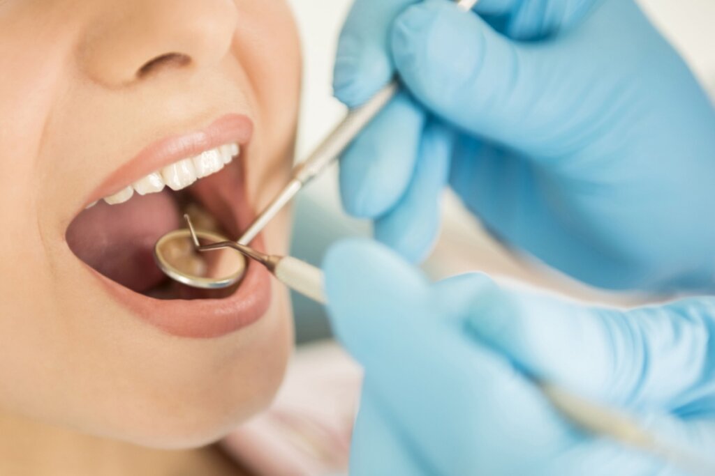 Mãos com luva azul examinando uma boca com equipamentos de metal 
