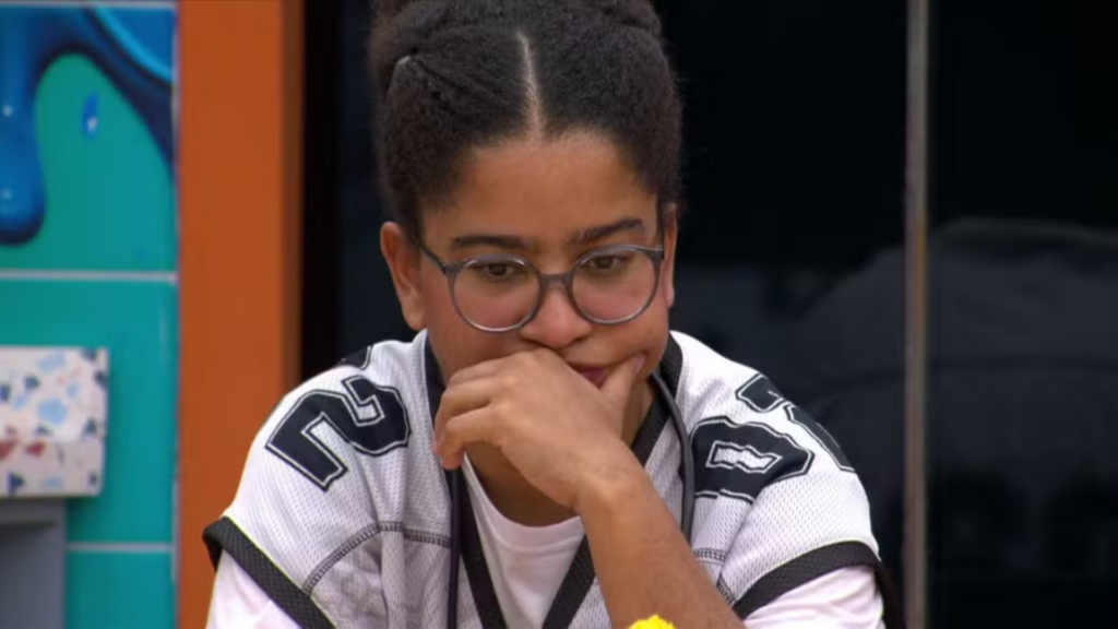 Milena pensativa com o rosto apoiado na mão