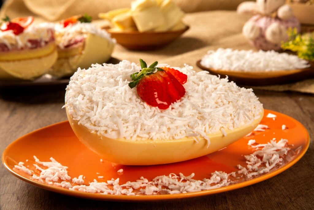 Ovo de Páscoa de chocolate branco recheado com beijinho, e com coco ralado por cima com morango em prato de cerâmica laranja em cima de mesa de madeira