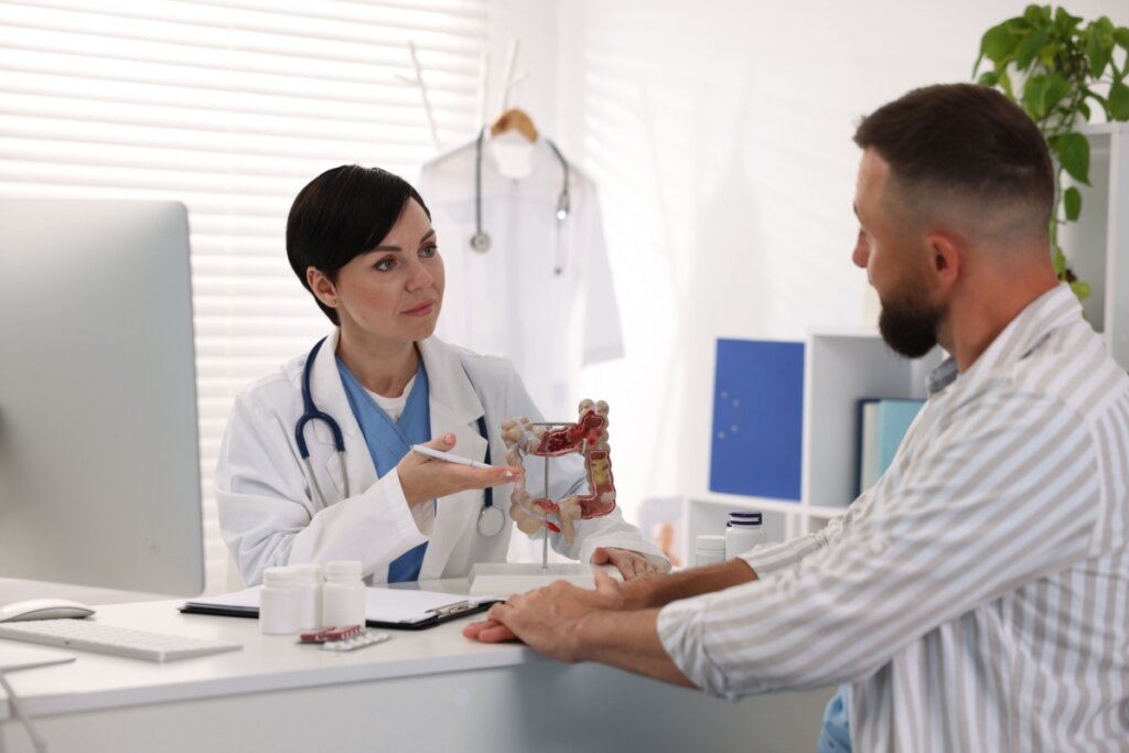 Médica atendendo um homem em um consultório, com a anatomia de um intestino na mesa, ambos sentados