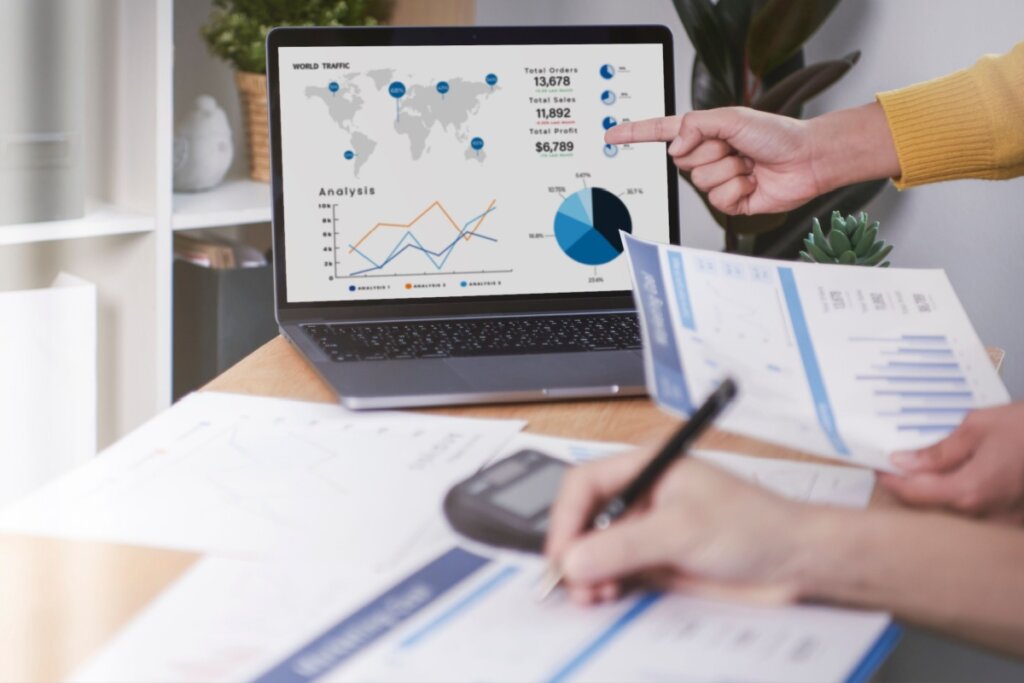 Computador com gráficos e mãos segurando papéis também com gráficos