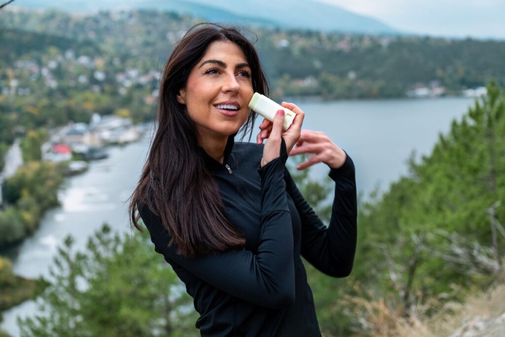 Mulher usando blusa de frio preta e passando protetor solar no rosto 