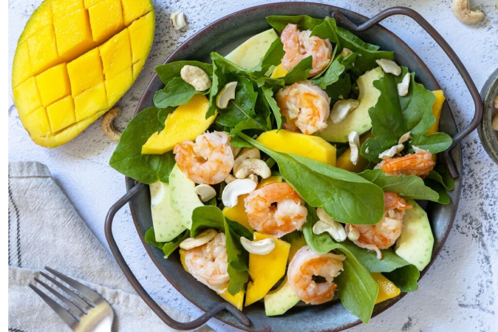 Recipiente preto com salada de rúcula, camarão, manga e abacate