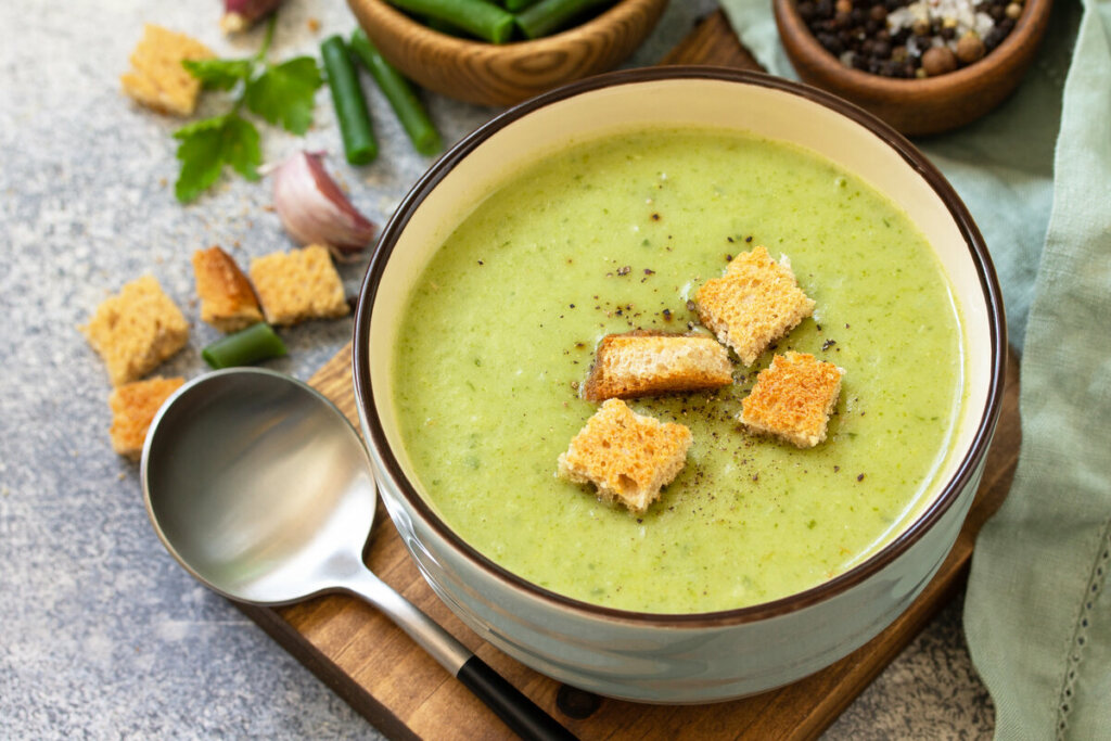 Panela branca com sopa de espinafre em cima de uma tábua de madeira