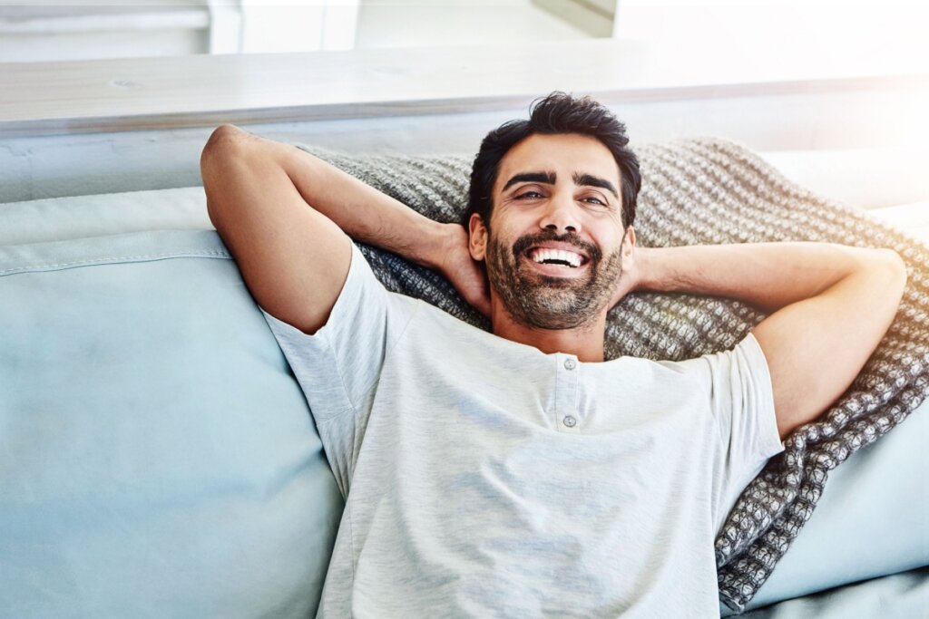 Homem relaxando sorrindo no sofá com as mãos atrás da cabeça