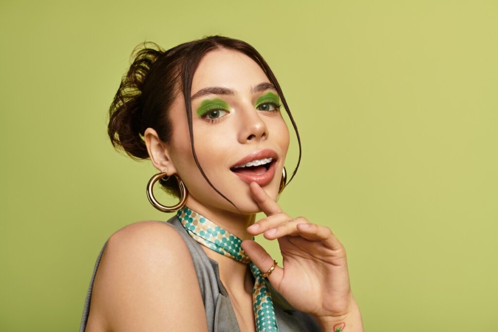 Mulher com maquiagem de sombra verde-oliva posando em frente a fundo verde