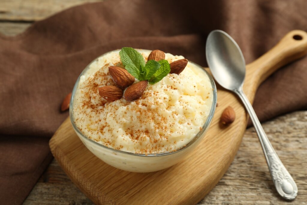 Recipiente de vidro com arroz doce com amêndoas e creme de baunilha em uma tábua de madeira e colher de metal do lado