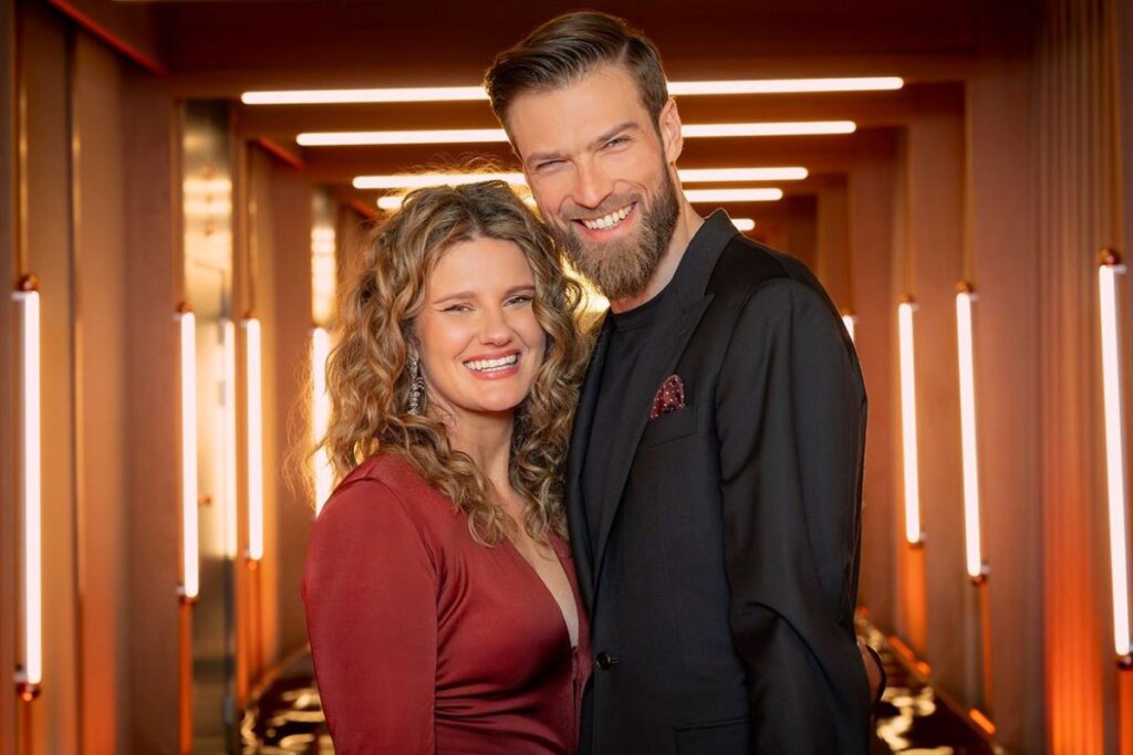Casal de apresentadores de "Casamento às Cegas: Polônia" lado a lado e sorrindo 