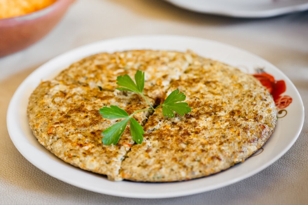 Frittata de quinoa decorada com salsinha em prato branco dividida em quatro pedaços