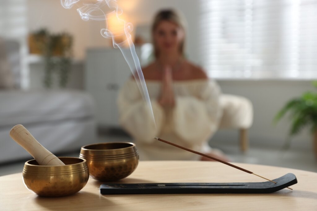Incenso aceso em cima de uma mesa com uma mulher sentada meditando ao fundo