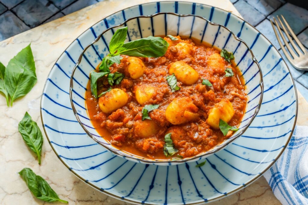 Nhoque de batata com lentilha ao molho de tomate servido em prato decorado com folhas de manjericão fresco