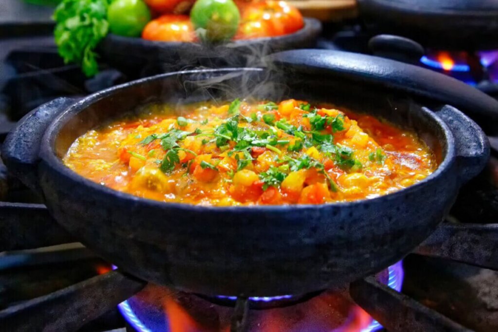 Moqueca na panela preta em cima do fogão com cebolinha