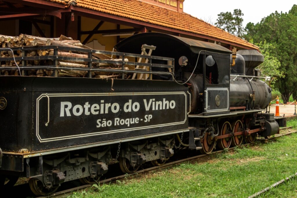 Trem antigo com uma placa escrito Roteiro do Vinho São Roque 