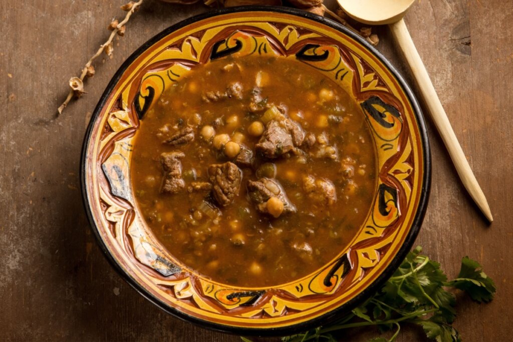 Sopa marroquina com cubos de carne e grão-de-bico servida em tigela decorada sobre mesa de madeira