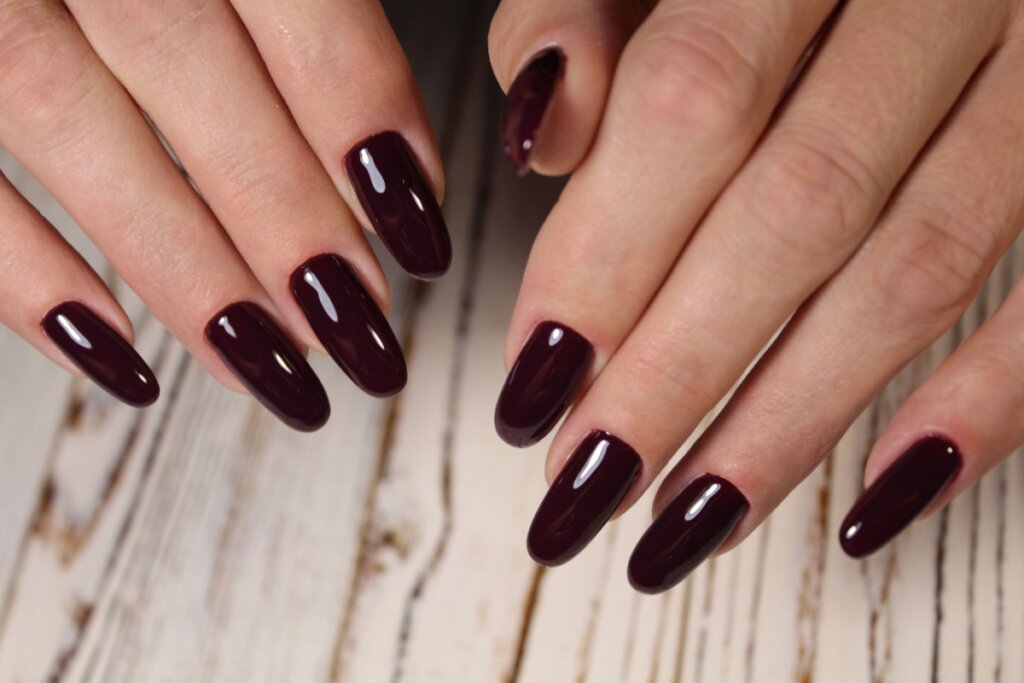 Mãos com unhas longas pintadas com esmalte vinho