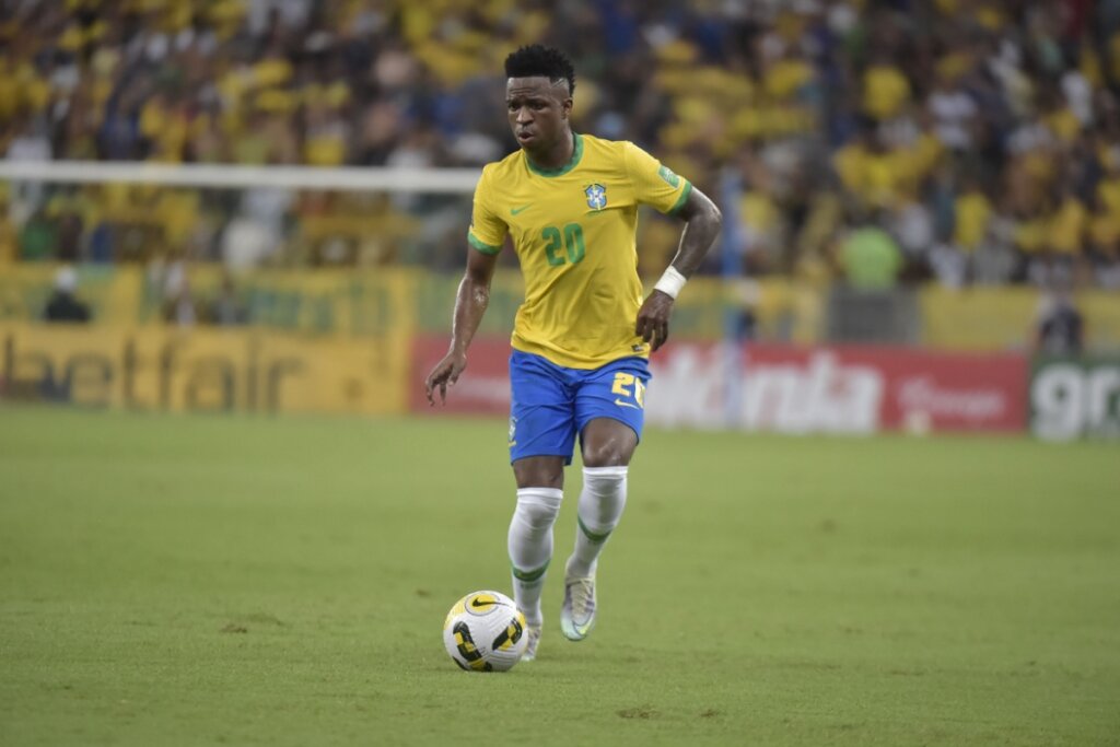 Vinícius Júnior jogando bola em campo usando a camisa da seleção brasileira