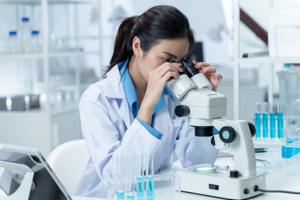 Biomédica sentada e fazendo análise em um microscopio