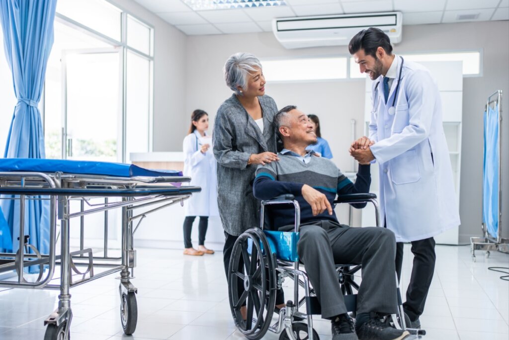 Médico conversando com um homem em uma cadeira de rodas e uma mulher segurando a cadeira