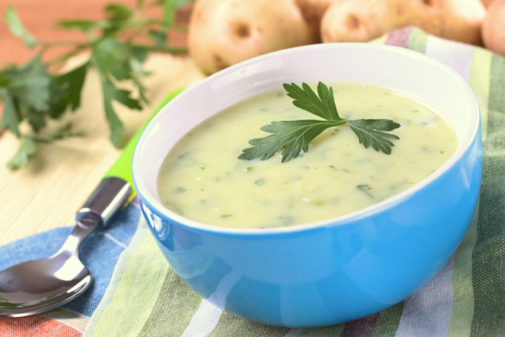 Caldo verde saudável servido em tigela azul com fundo branco em cima de toalha listrada verde em cima de mesa de madeira