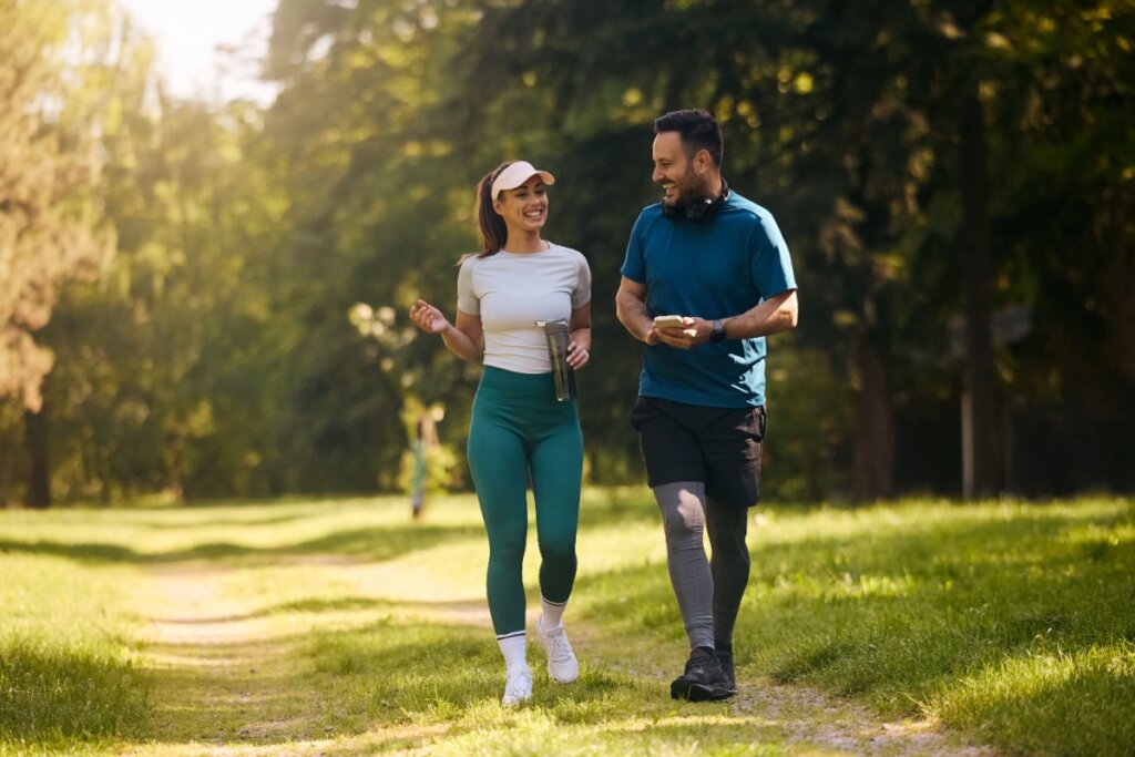 Homem e mulher com roupas esportivas praticando caminhada em ambiente verde aberto