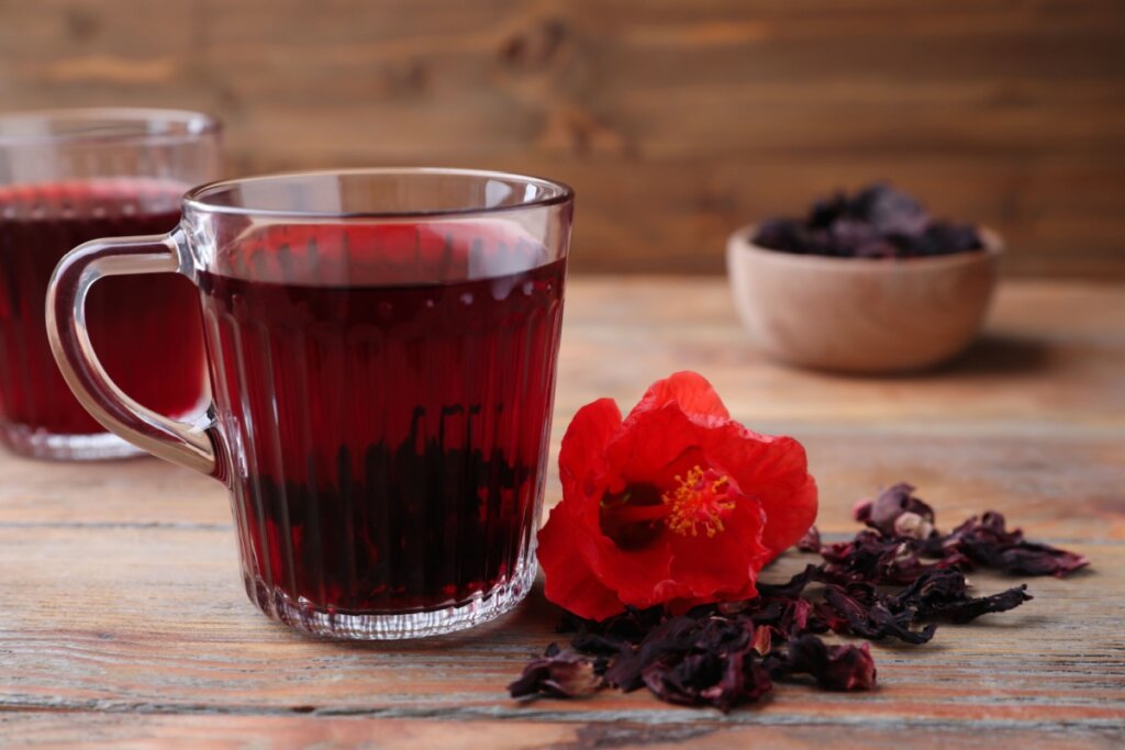 duas canecas de vidro com chá vermelho de hibisco e flores de hibisco ao lado