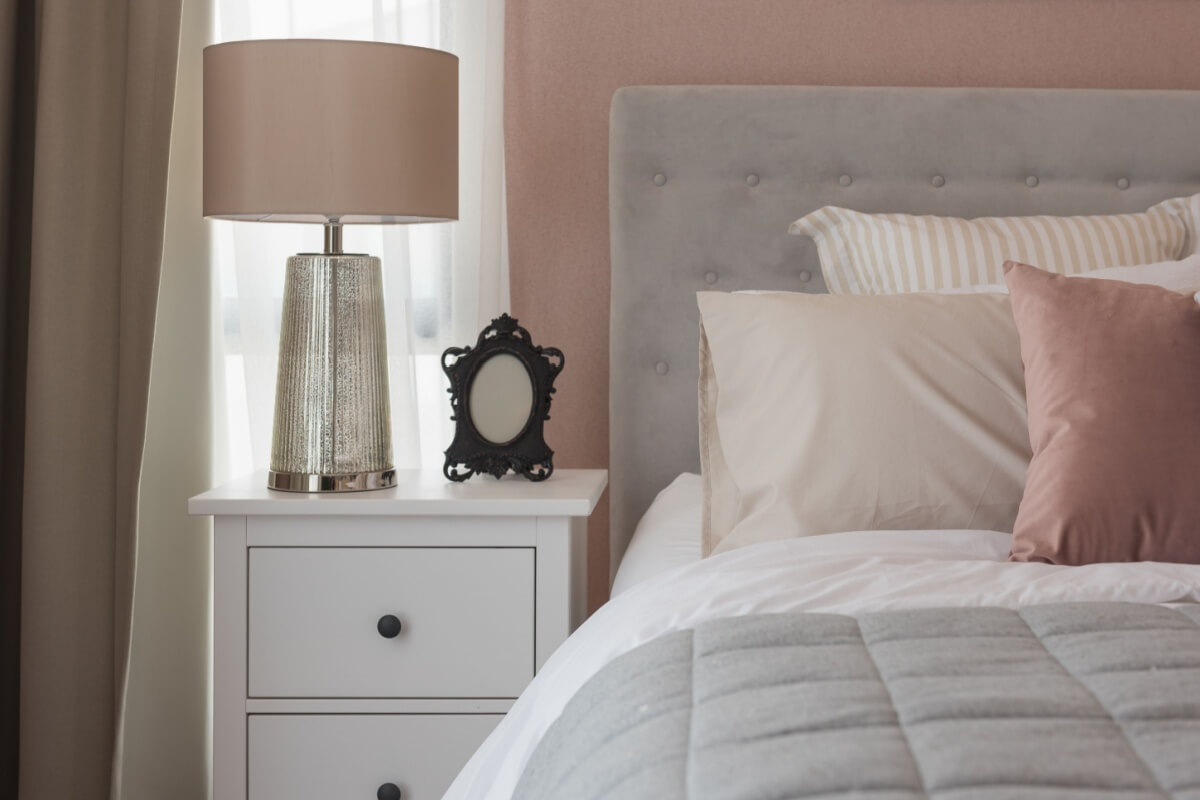 Mesa de cabeceira ao lado de uma cama com forro em tons de cinza, rosa e branco 