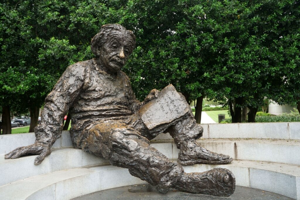 Estátua de Albert Einstein sentado e lendo um livro em uma praça 