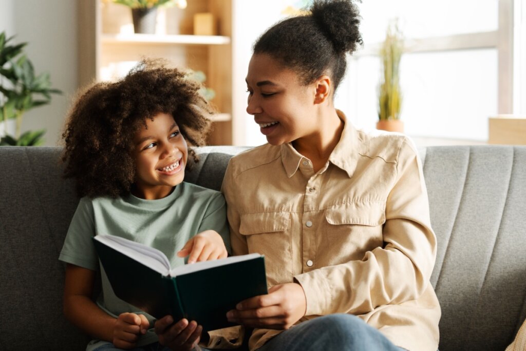 Mãe e filho sorrindo enquanto leem juntos um livro no sofá de casa