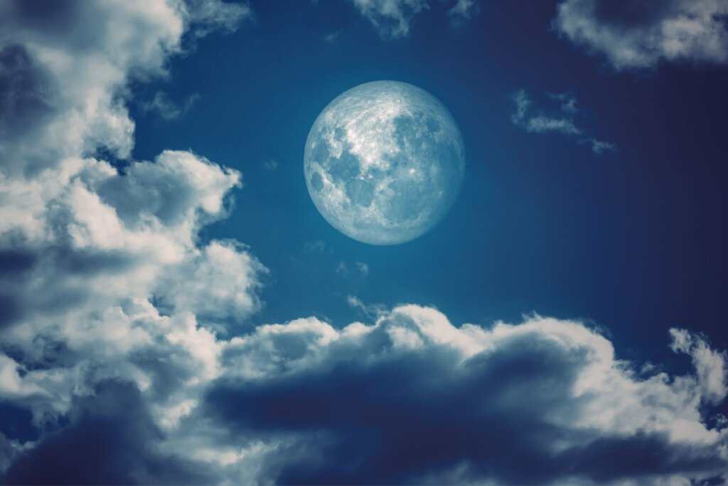 imagem da lua cheia em céu azul com nuvens brancas