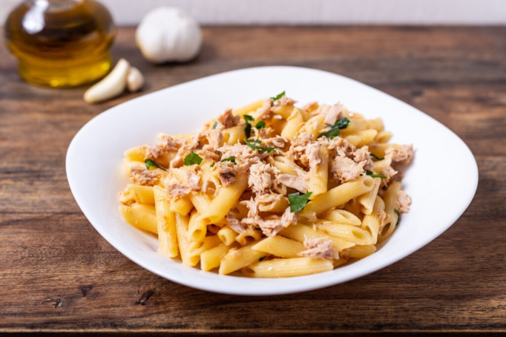 Macarrão com manteiga e atum em um prato branco sobre uma mesa de madeira 