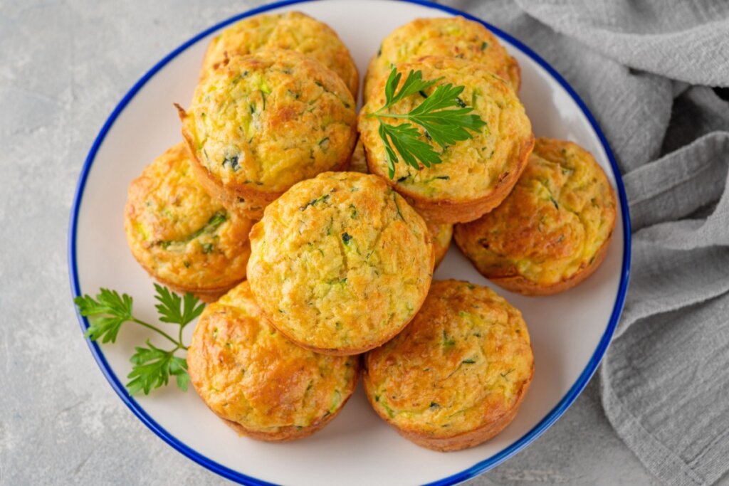 Muffins de ovo com vegetais servido em prato branco com borda azul em cima de mesa de pedra