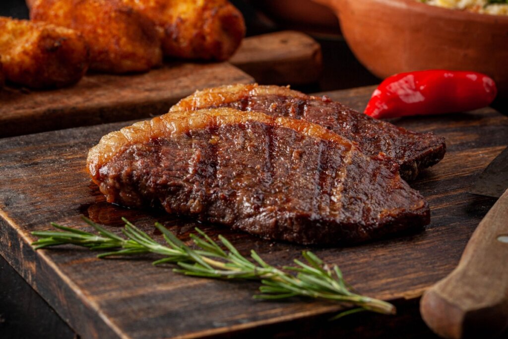 Dois pedaços de picanha na manteiga em uma tábua de madeira. Ao lado, ramo de alecrim 