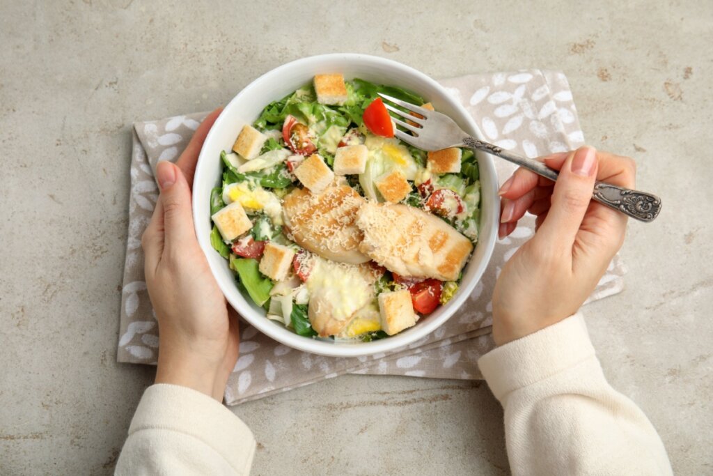 prato branco com salada com alface e frango. duas mãos em volta