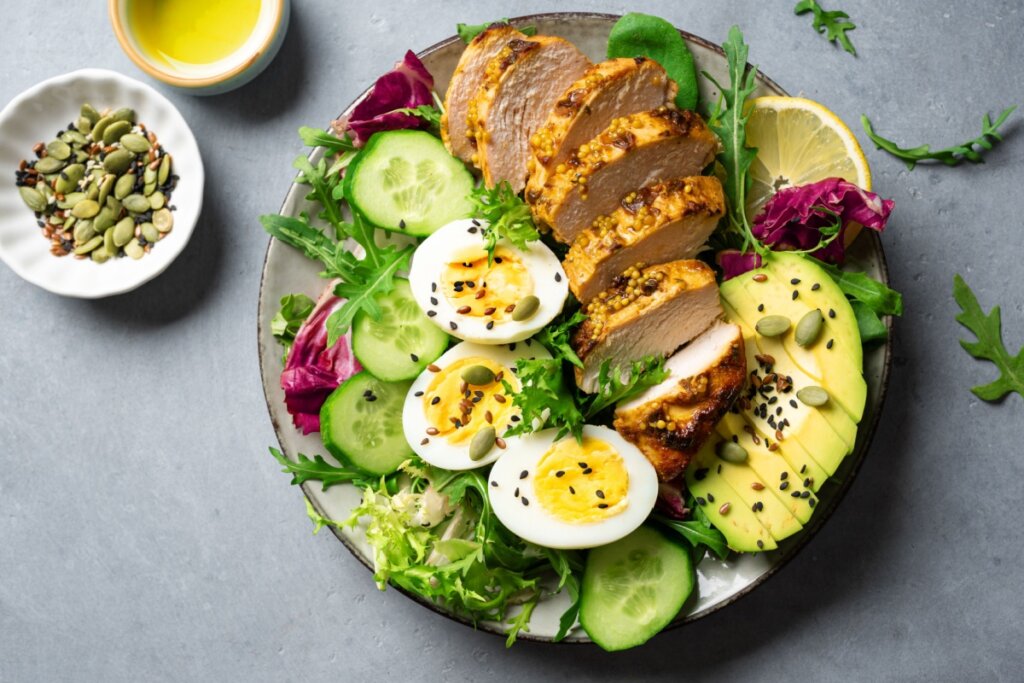 Salada de peito de frango com ovos e abacate servida em prato raso em cima de bancada de pedra