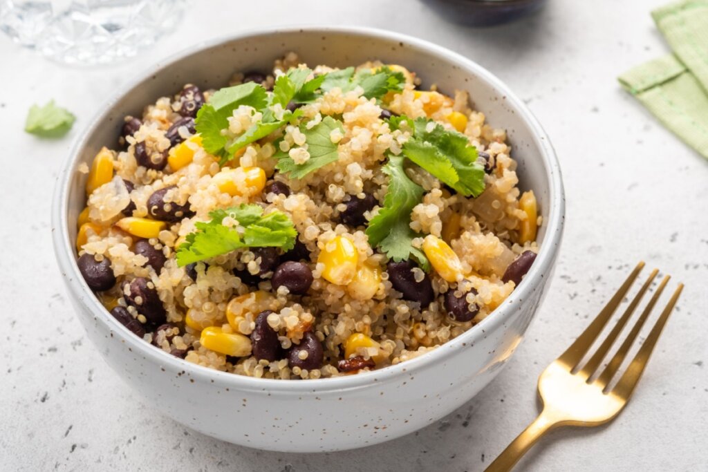 Salada de quinoa com feijão-preto e milho servida em tigela branca em cima de bancada de pedra branca 