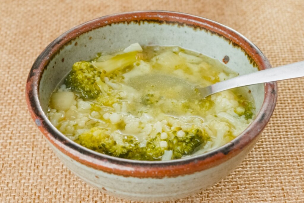 Sopa de brócolis com couve-flor em tigela de cerâmica em cima de mesa com toalha de estopa 