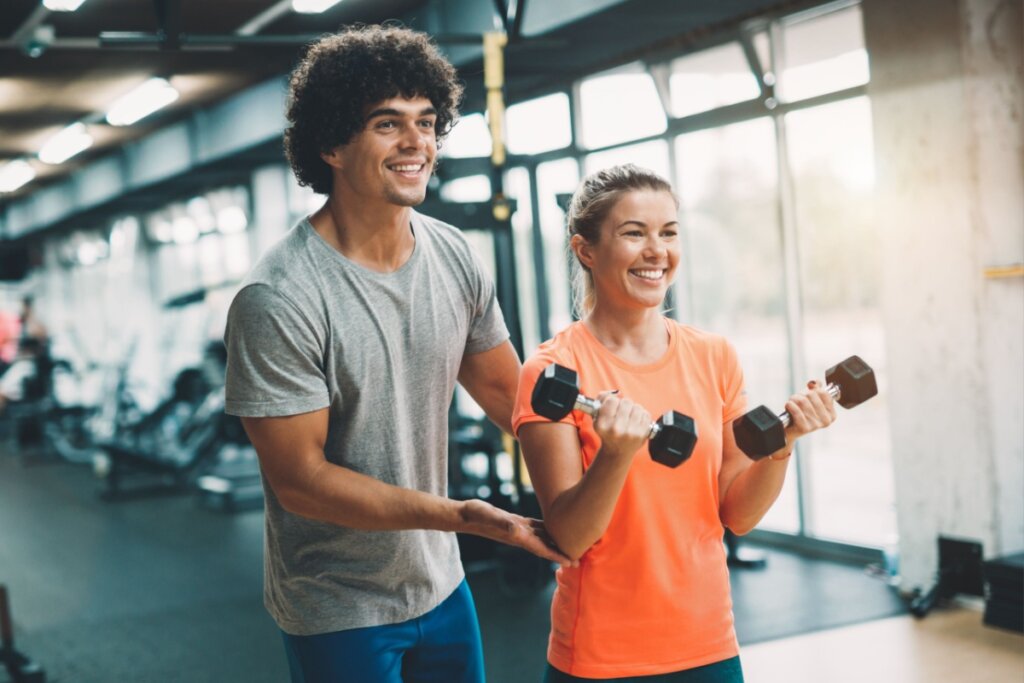 Mulher em uma academia, fazendo musculação com a ajuda de personal trainer