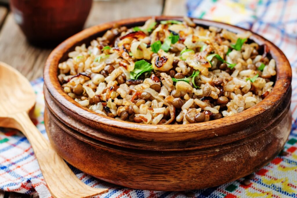 Arroz com lentilhas e cebolas douradas servido em recipiente de madeira