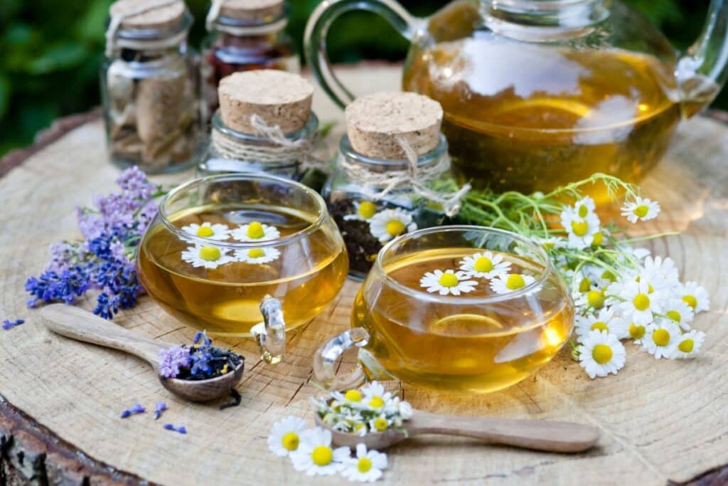 Xícaras e bule de chá de camomila com flores frescas de camomila e ramos de lavanda dispostos