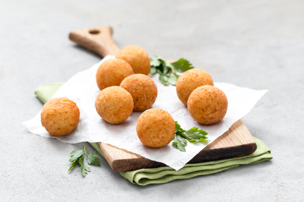 Croquettes de fromage em cima de papel-manteiga, sobre tábua e pano verde 