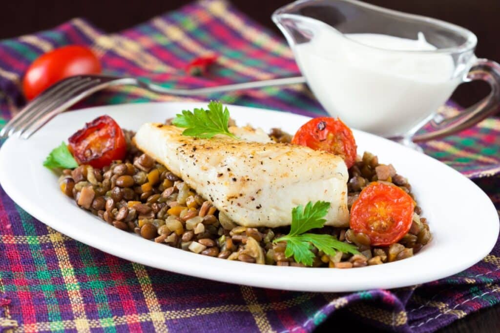 Prato branco com salada de lentilha, filé de peixe e tomates confitados