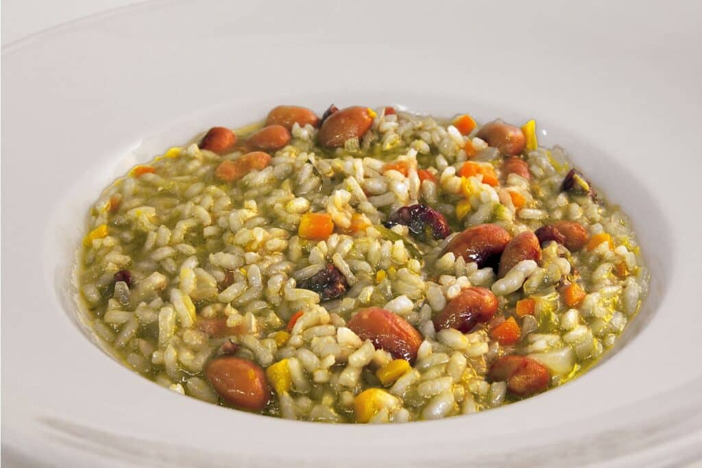 Risoto verde cremoso com feijão-borlotti cenoura em cubinhos, servido em prato fundo branco