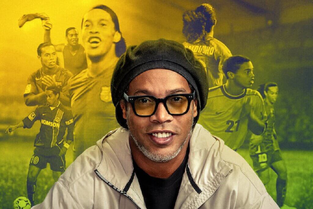 Uma imagem de rosto de Ronaldinho Gaúcho, um dos jogadores de futebol mais habilidosos de todos os tempos, com óculos de sol pretos e uma boina preta. Ele está sorrindo para a câmera. O fundo é uma imagem borrada de sua carreira.