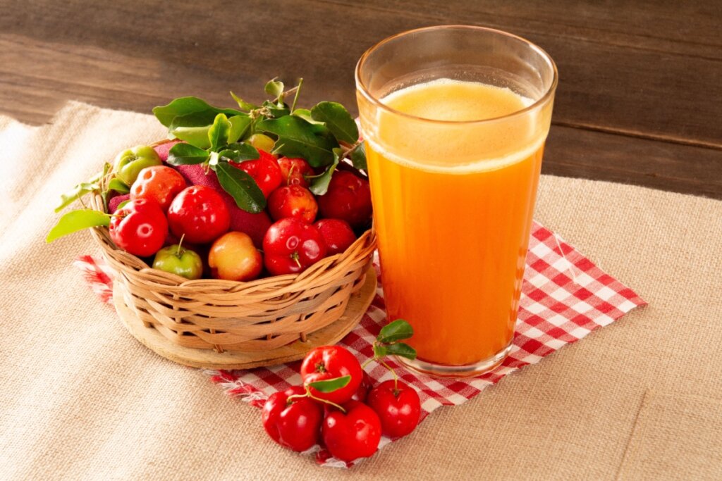 copo de vidro com suco laranja ao lado de cesto de palha com diversas acerolas