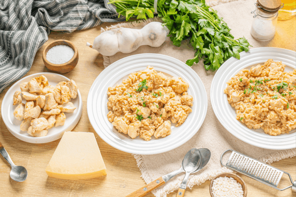 A imagem mostra um prato de arroz cremoso com frango, servido de forma caseira e apetitosa. O preparo aparece com grãos bem envolvidos por um molho cremoso, cubos de frango distribuídos por todo o prato e um toque de salsinha por cima.