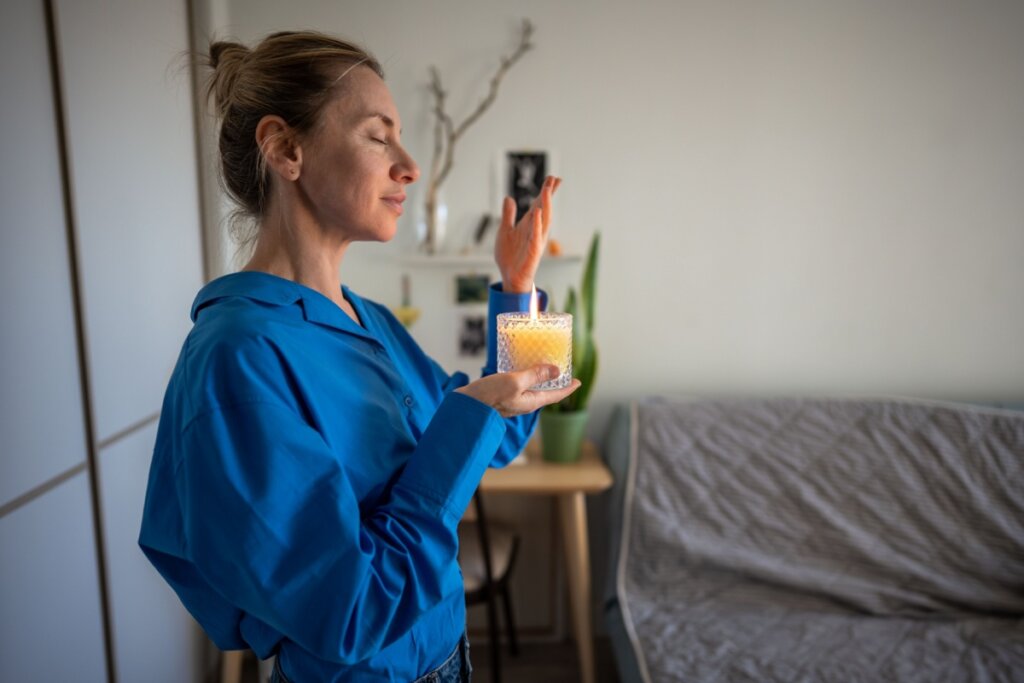 Mulher com expressão serena, usando camisa azul, segurando com uma mão um recipiente com vela amarela