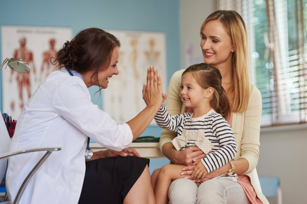 Médica fazendo high five com uma menina sentada no colo de outra mulher